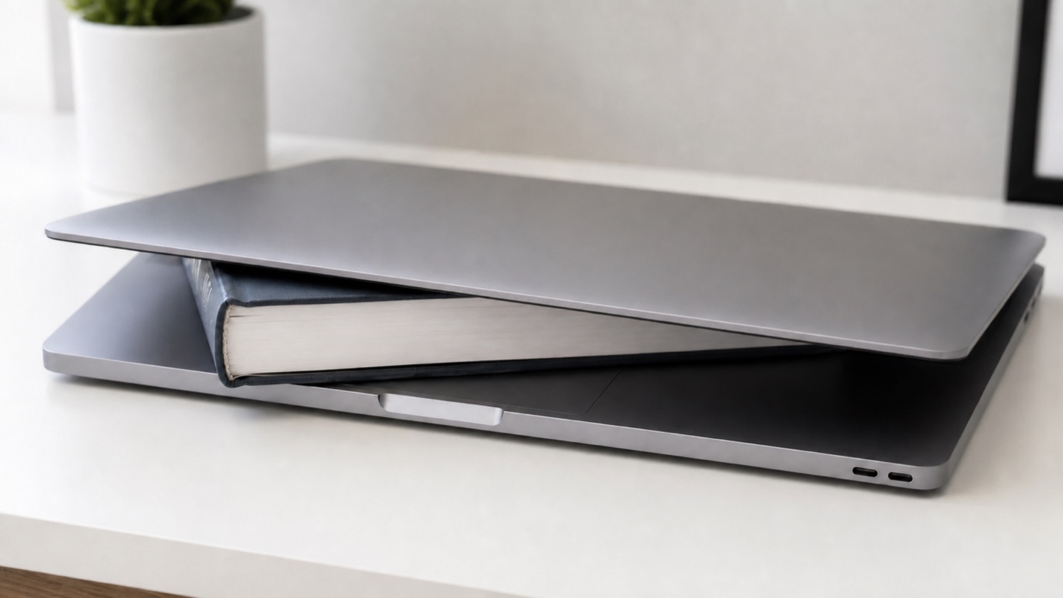 A book wedged in a nearly-closed MacBook on a clean desk, propping the lid open a crack — the hack lidawake replaces.
